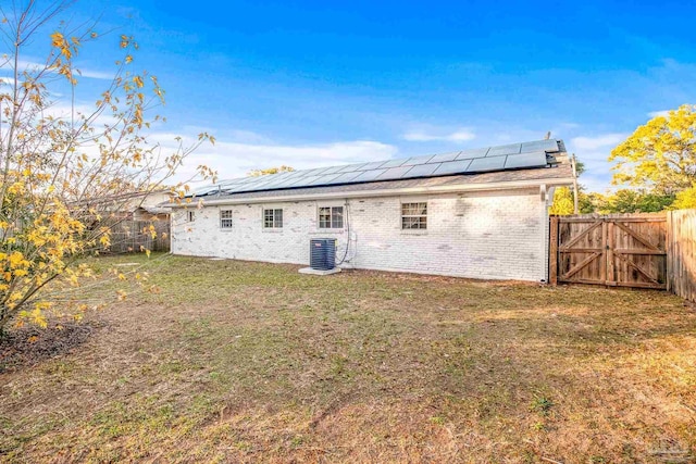 rear view of property with a yard, central AC unit, and solar panels