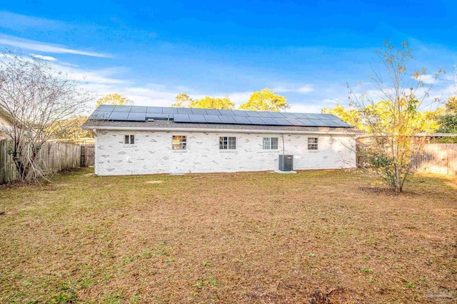 rear view of house featuring a lawn, central AC unit, and solar panels