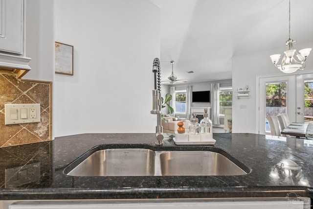 kitchen with ceiling fan with notable chandelier, a fireplace, a sink, tasteful backsplash, and pendant lighting