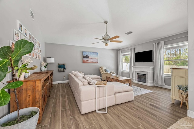 living area with baseboards, visible vents, wood finished floors, and a glass covered fireplace