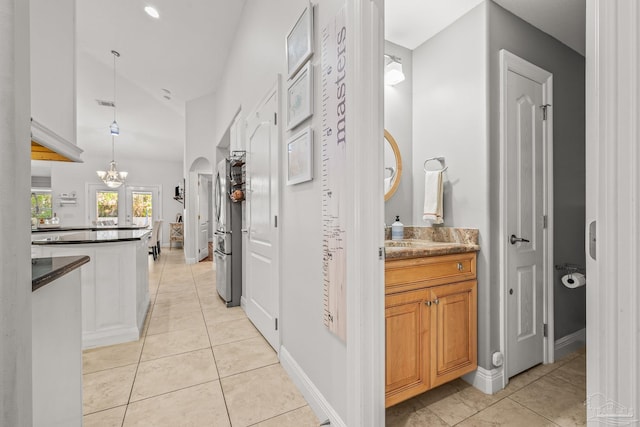 hallway with a chandelier, arched walkways, baseboards, and light tile patterned floors