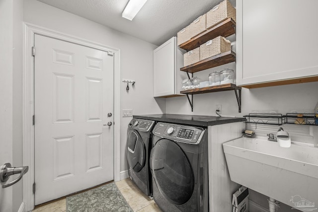 clothes washing area with cabinet space, a textured ceiling, separate washer and dryer, and a sink