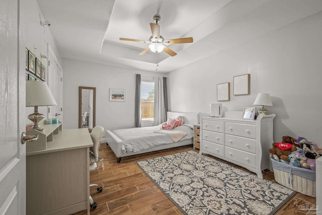 bedroom with wood finished floors, a raised ceiling, and a ceiling fan