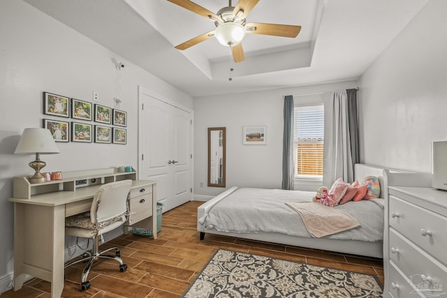 bedroom with baseboards, ceiling fan, a raised ceiling, and wood tiled floor