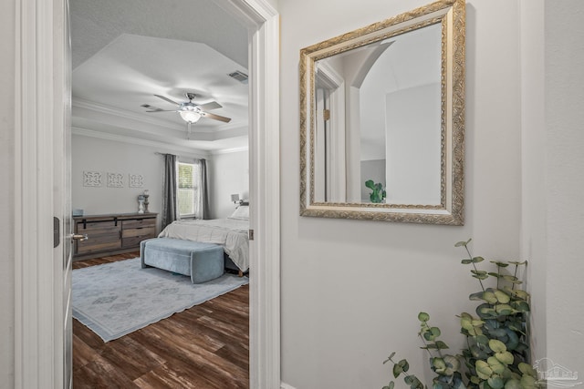 bedroom featuring dark wood-type flooring, a ceiling fan, visible vents, a tray ceiling, and crown molding