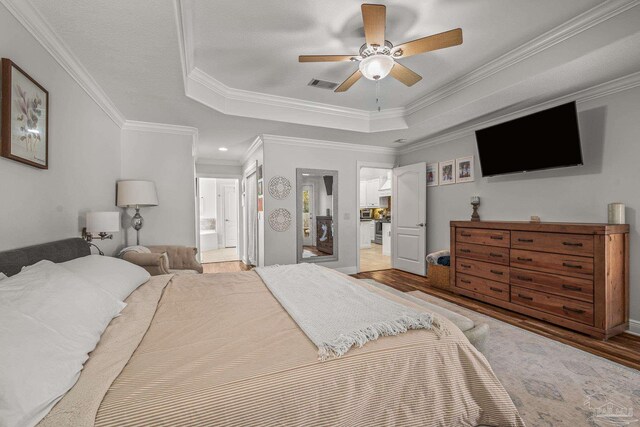 bedroom featuring crown molding, a raised ceiling, visible vents, connected bathroom, and wood finished floors