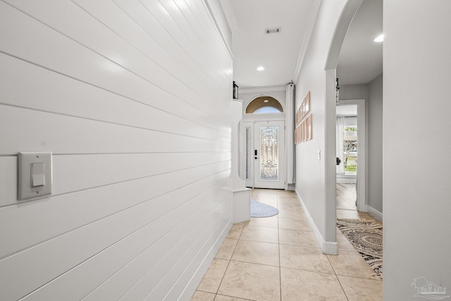 doorway with arched walkways, crown molding, recessed lighting, light tile patterned flooring, and baseboards