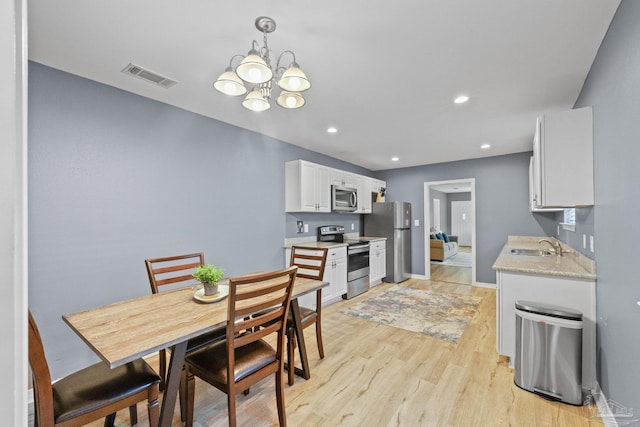 dining room with sink, light hardwood / wood-style flooring, and a notable chandelier