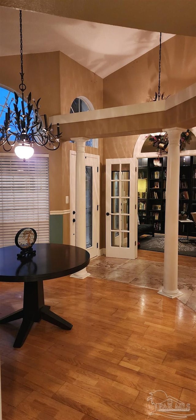 unfurnished dining area with wood finished floors, ornate columns, arched walkways, a towering ceiling, and an inviting chandelier