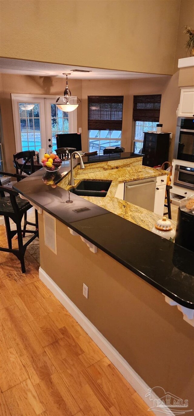 kitchen featuring white cabinetry, stainless steel dishwasher, dark stone counters, a sink, and light wood-style floors