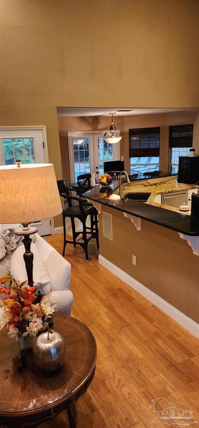 kitchen with dark countertops, a sink, light wood-type flooring, a high ceiling, and a kitchen breakfast bar