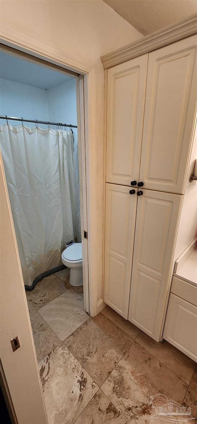 bathroom featuring a shower with curtain, stone finish floor, and toilet