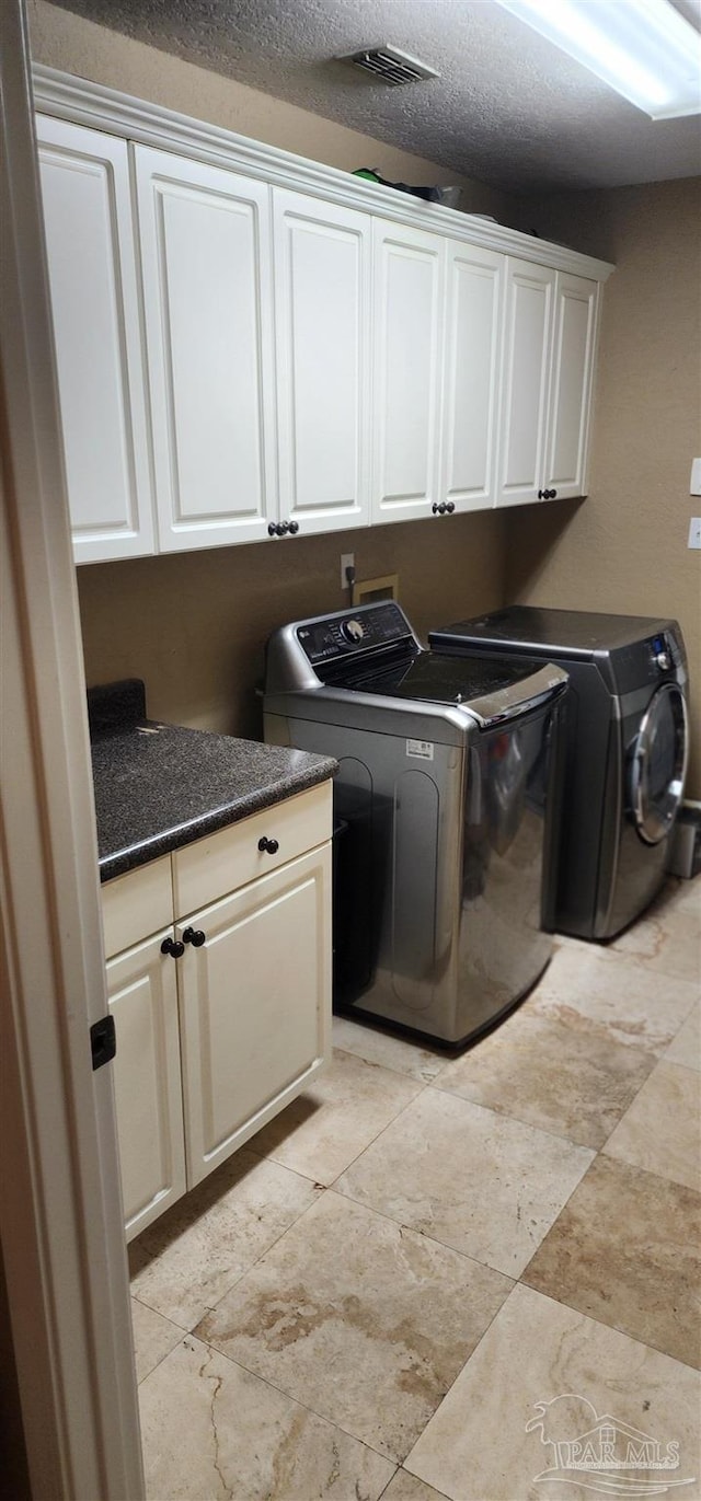 washroom with a textured ceiling, cabinet space, washing machine and dryer, and visible vents