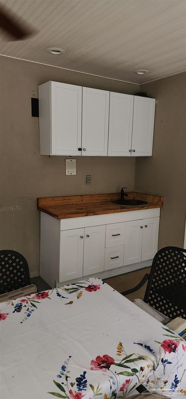 kitchen with white cabinetry, a sink, butcher block counters, and wood ceiling