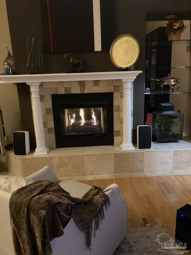 living room with decorative columns, a tiled fireplace, and wood finished floors