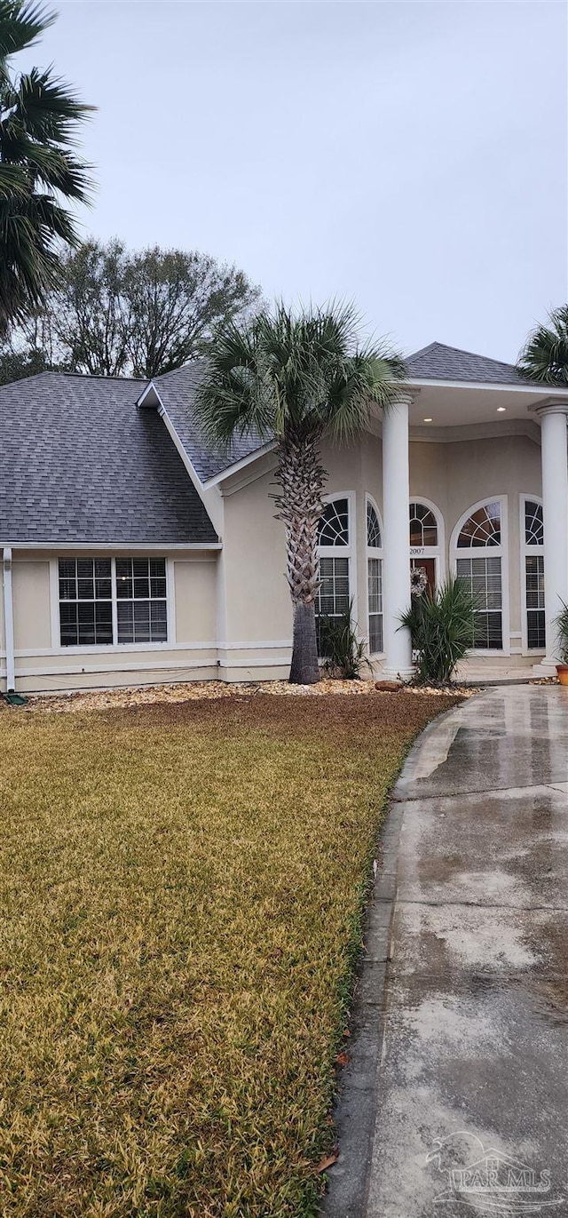 view of front facade featuring a front lawn, a shingled roof, stucco siding, and concrete driveway