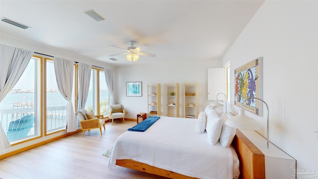 bedroom featuring ceiling fan, multiple windows, light hardwood / wood-style flooring, and a water view