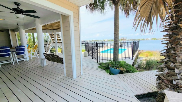 wooden terrace with a water view, a fenced in pool, and ceiling fan