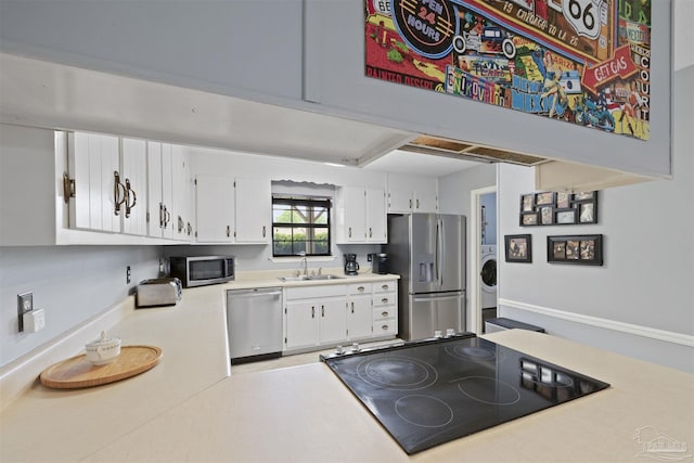 kitchen with light countertops, appliances with stainless steel finishes, washer / dryer, and white cabinetry
