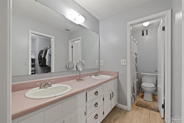 bathroom featuring double vanity, wood finished floors, toilet, and a sink