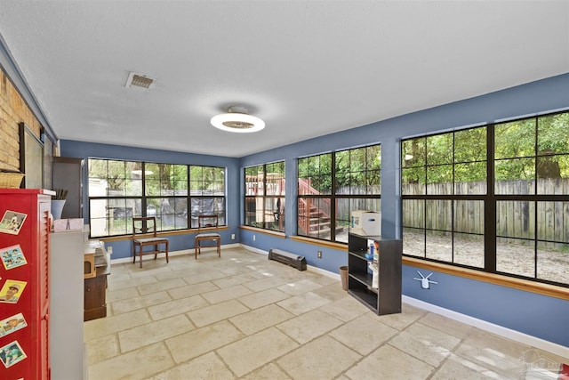unfurnished sunroom with baseboards, stone tile floors, and visible vents