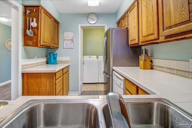 kitchen featuring tile countertops, white dishwasher, a textured ceiling, and independent washer and dryer