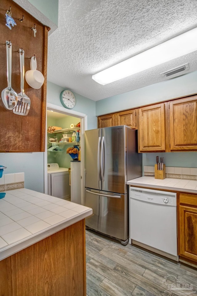 kitchen with light hardwood / wood-style flooring, stainless steel fridge, tile counters, white dishwasher, and washing machine and dryer