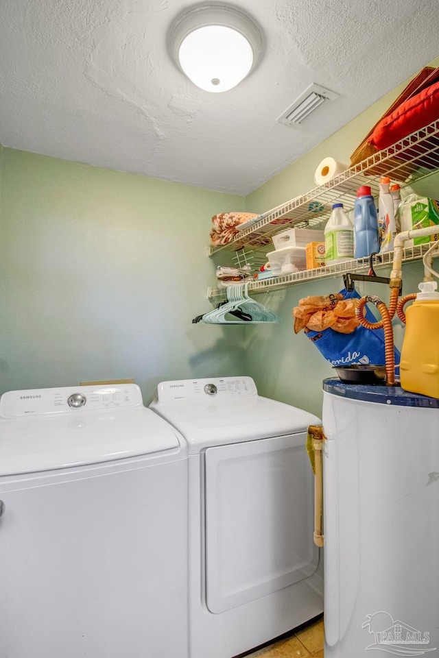 clothes washing area with light tile patterned floors, washer and clothes dryer, water heater, and a textured ceiling