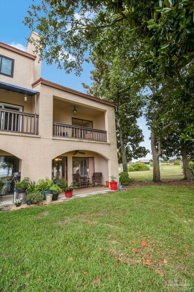 back of house featuring ceiling fan, a lawn, a patio, and a balcony