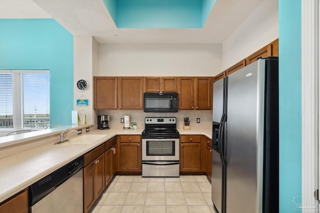 kitchen featuring sink, appliances with stainless steel finishes, a tray ceiling, light tile patterned flooring, and decorative backsplash