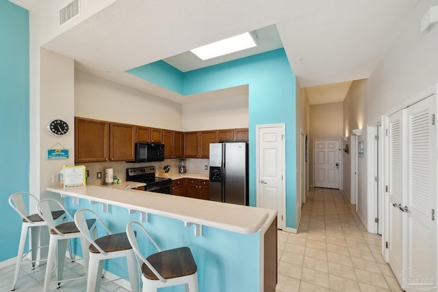 kitchen with a towering ceiling, tasteful backsplash, light tile patterned floors, kitchen peninsula, and stainless steel appliances