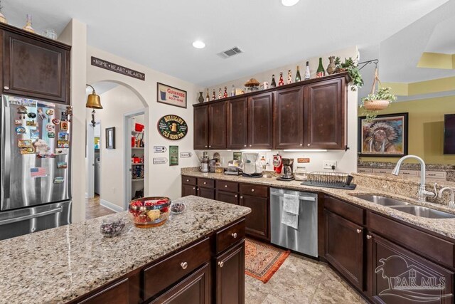 kitchen featuring sink, light stone countertops, dark brown cabinetry, and stainless steel appliances