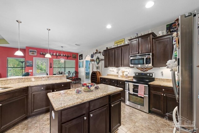 kitchen with light stone countertops, appliances with stainless steel finishes, a center island, hanging light fixtures, and dark brown cabinetry