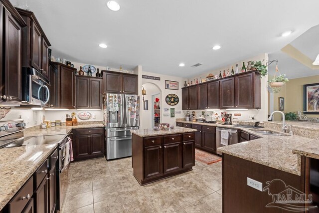 kitchen featuring dark brown cabinets, stainless steel appliances, light stone countertops, and sink