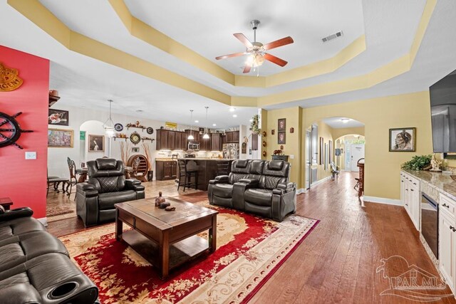 living room featuring a tray ceiling, wood-type flooring, and ceiling fan