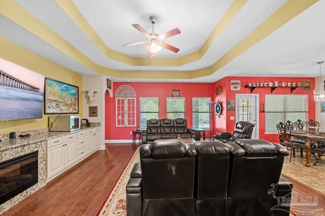 living room with ceiling fan, a tray ceiling, and dark hardwood / wood-style flooring