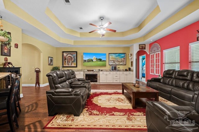 living room featuring ceiling fan, wood-type flooring, and a tray ceiling