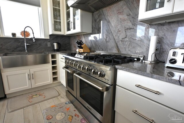 kitchen featuring backsplash, dark stone counters, range with two ovens, white cabinets, and custom exhaust hood