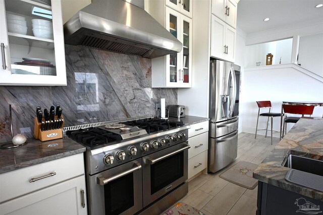 kitchen featuring white cabinets, wall chimney range hood, stainless steel appliances, and tasteful backsplash