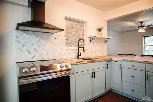 kitchen with butcher block countertops, sink, backsplash, stainless steel range with electric cooktop, and wall chimney exhaust hood