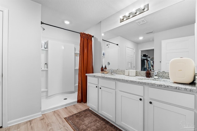 bathroom with wood-type flooring, vanity, a textured ceiling, and walk in shower