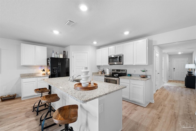 kitchen with a kitchen bar, white cabinetry, an island with sink, and stainless steel appliances