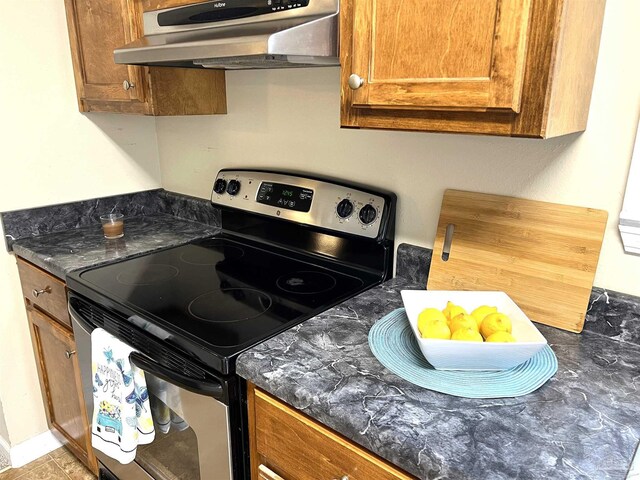 kitchen featuring range hood, dark stone counters, and stainless steel range with electric stovetop