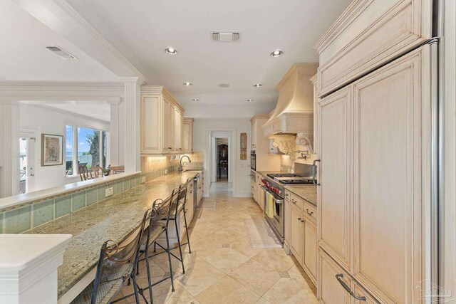 kitchen featuring a breakfast bar, appliances with stainless steel finishes, custom exhaust hood, and light stone countertops