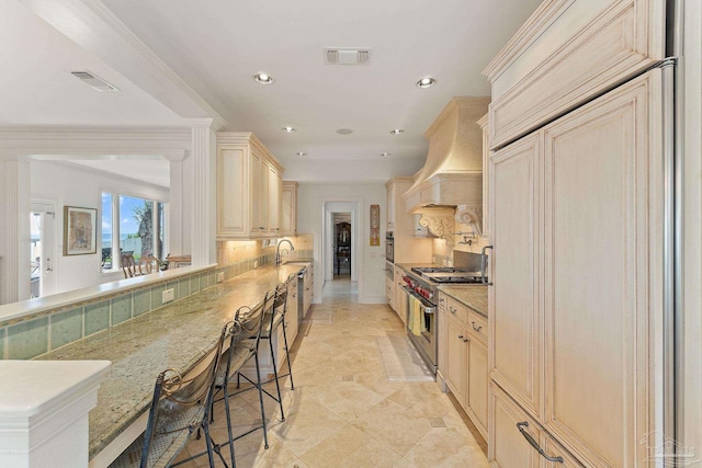 kitchen with visible vents, a breakfast bar, stainless steel stove, premium range hood, and backsplash