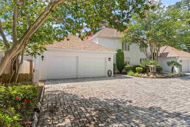 exterior space featuring decorative driveway, brick siding, roof with shingles, fence, and a garage