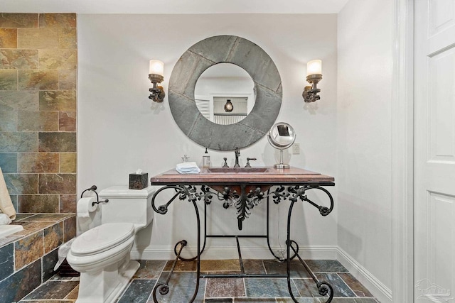 bathroom with toilet, a sink, stone tile flooring, and baseboards