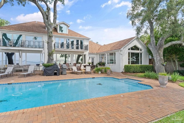 rear view of property featuring a patio, a balcony, brick siding, fence, and an outdoor pool