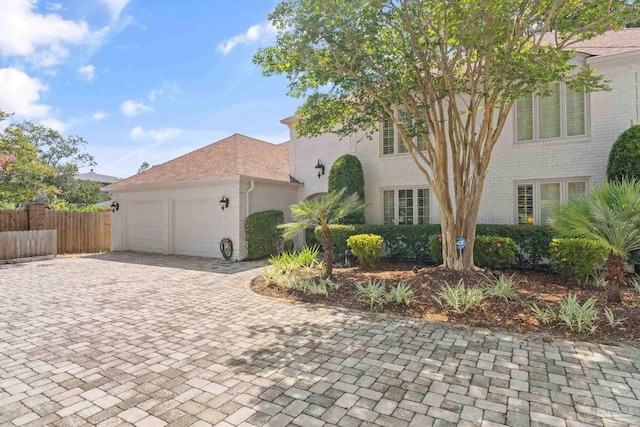 view of front facade with a garage, brick siding, decorative driveway, and fence