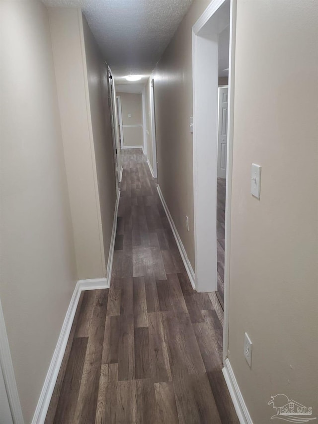 hallway featuring baseboards, dark wood-type flooring, and a textured ceiling